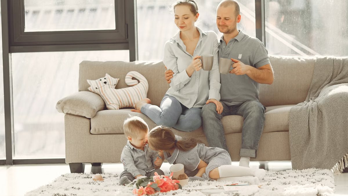 Cheerful family smiling while spending weekend together sitting parents sitting on comfortable sofa while children resting on carpet and playing